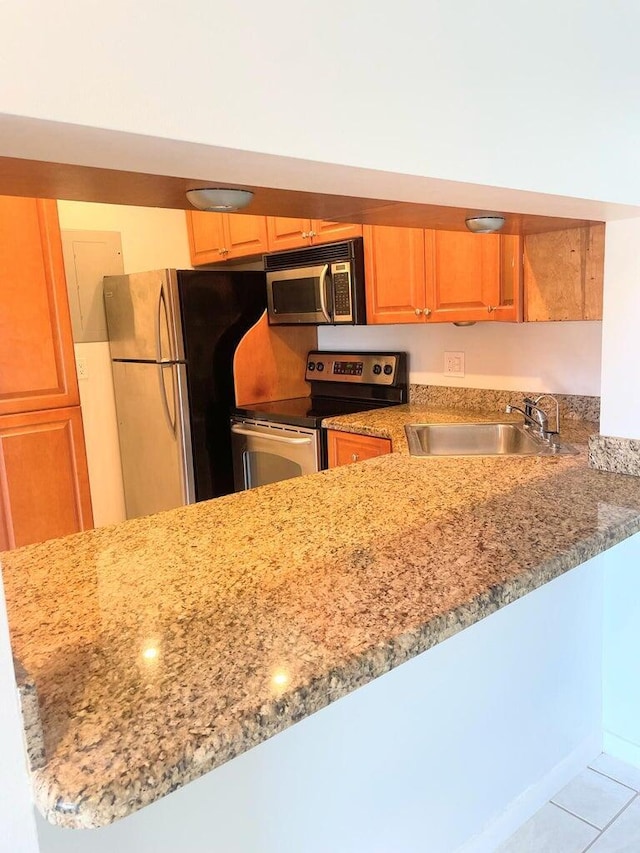 kitchen featuring light tile patterned floors, light stone counters, appliances with stainless steel finishes, and a sink