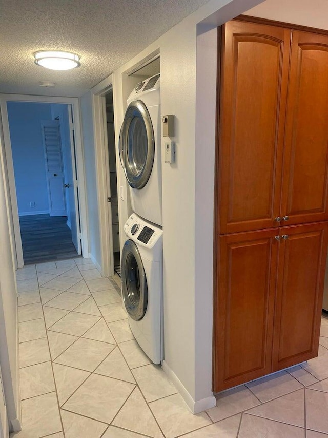 washroom with a textured ceiling, stacked washer / dryer, light tile patterned floors, baseboards, and laundry area