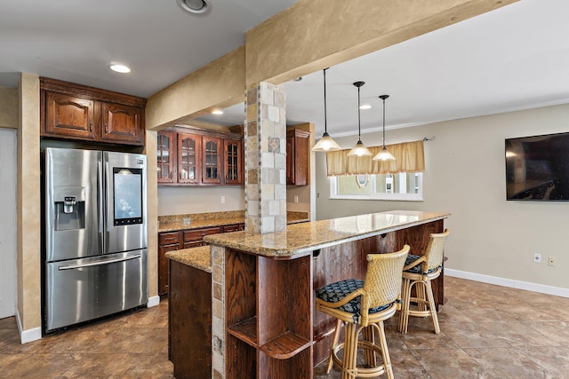 kitchen featuring glass insert cabinets, baseboards, a breakfast bar, light stone counters, and stainless steel refrigerator with ice dispenser