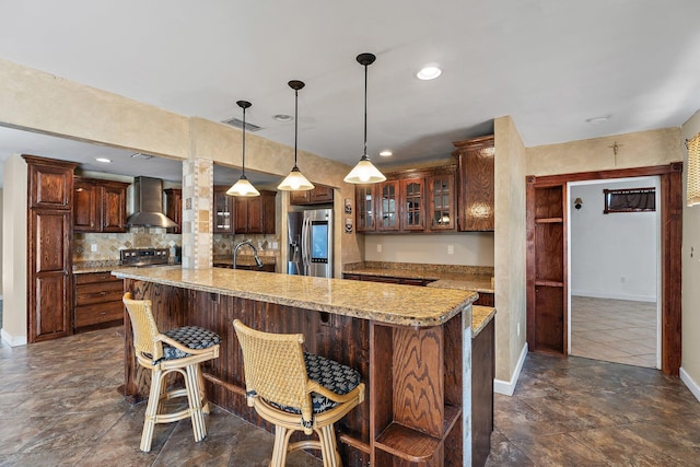 kitchen featuring a kitchen bar, a sink, wall chimney exhaust hood, stainless steel fridge with ice dispenser, and glass insert cabinets