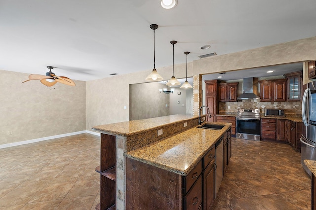 kitchen with a center island with sink, a sink, stainless steel appliances, wall chimney range hood, and decorative backsplash