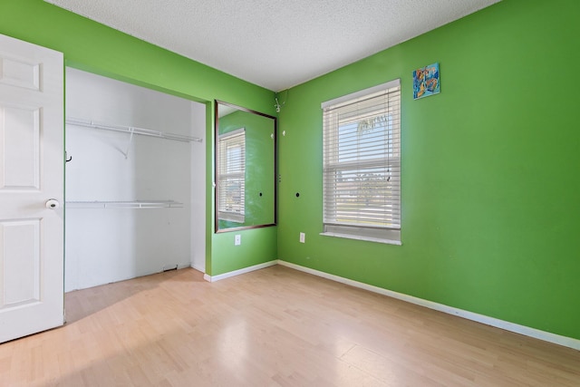 unfurnished bedroom featuring a closet, baseboards, a textured ceiling, and wood finished floors