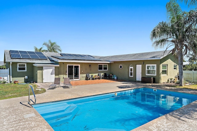 rear view of house with a fenced in pool, fence, roof mounted solar panels, stucco siding, and a patio