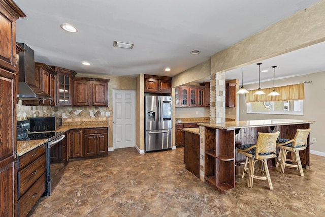 kitchen with a breakfast bar area, wall chimney exhaust hood, glass insert cabinets, and appliances with stainless steel finishes