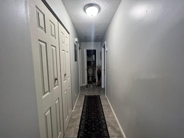 hall featuring light tile patterned floors, attic access, a textured ceiling, and baseboards