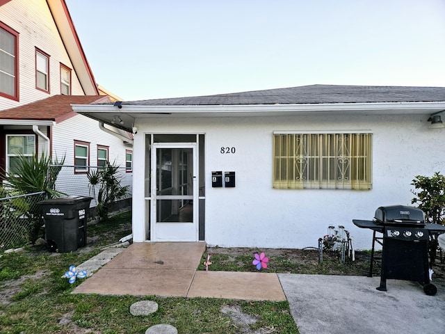 entrance to property with fence, roof with shingles, and stucco siding