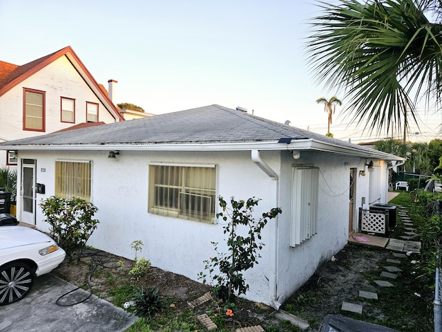 view of side of home featuring a shingled roof, central AC unit, and stucco siding