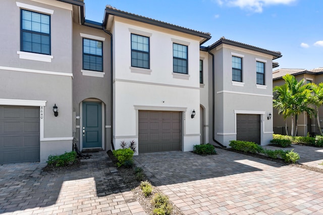 view of property featuring stucco siding, an attached garage, a tile roof, and decorative driveway