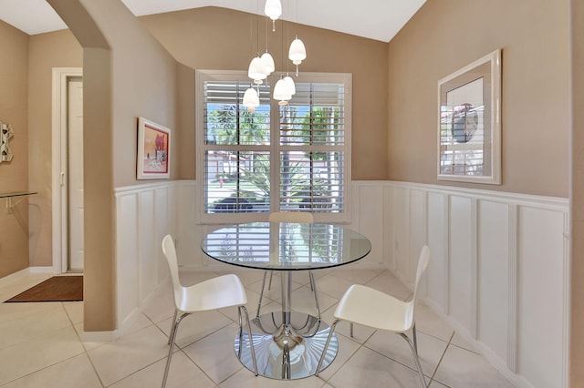 dining space featuring a wainscoted wall, vaulted ceiling, light tile patterned floors, arched walkways, and a notable chandelier