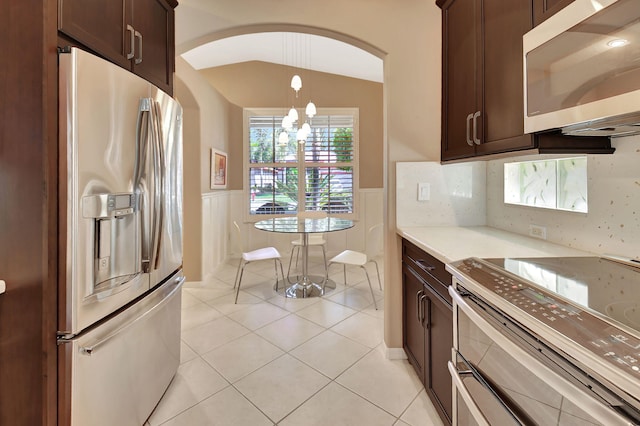 kitchen with arched walkways, appliances with stainless steel finishes, wainscoting, light countertops, and light tile patterned floors