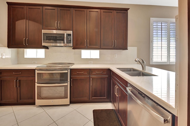 kitchen featuring light countertops, light tile patterned floors, decorative backsplash, appliances with stainless steel finishes, and a sink