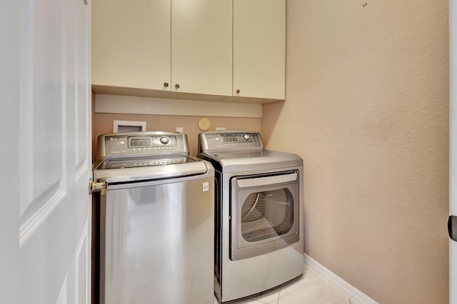 clothes washing area featuring light tile patterned flooring, cabinet space, baseboards, and separate washer and dryer