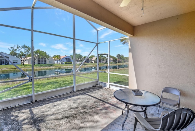 unfurnished sunroom with a residential view, ceiling fan, and a water view