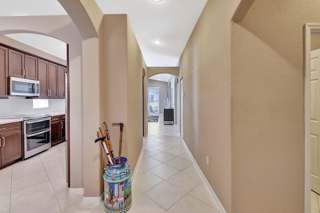 hall featuring light tile patterned flooring, baseboards, arched walkways, and a textured wall