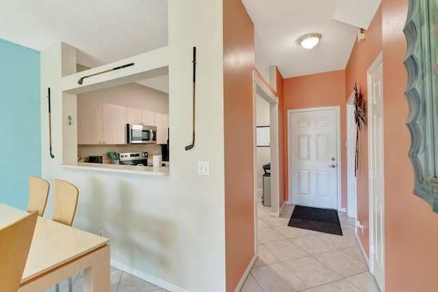 hall with lofted ceiling, light tile patterned floors, and baseboards