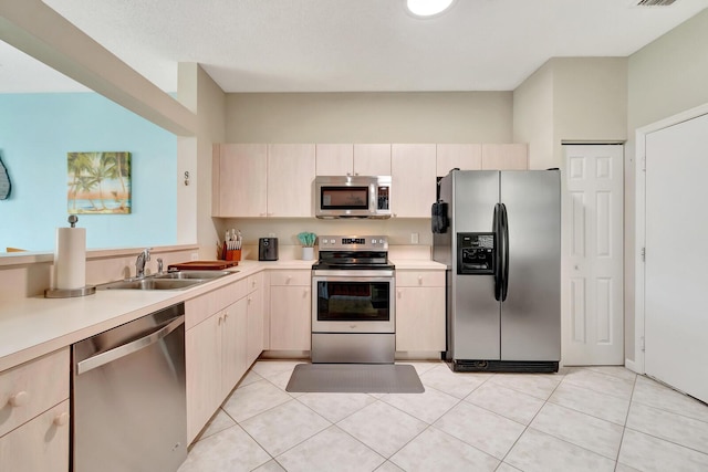 kitchen featuring light brown cabinets, light countertops, light tile patterned floors, appliances with stainless steel finishes, and a sink