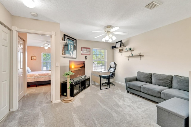 carpeted living area featuring baseboards, a ceiling fan, visible vents, and a textured ceiling