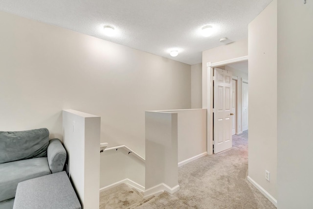 hallway with baseboards, an upstairs landing, a textured ceiling, and carpet flooring