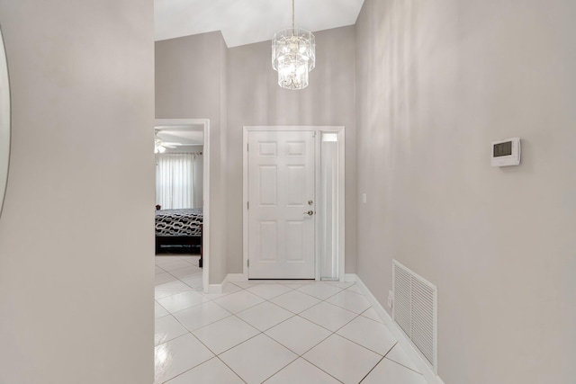 foyer entrance with visible vents, a notable chandelier, light tile patterned floors, baseboards, and a towering ceiling