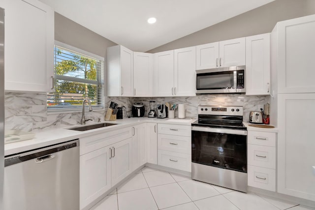 kitchen with lofted ceiling, a sink, light countertops, appliances with stainless steel finishes, and white cabinetry