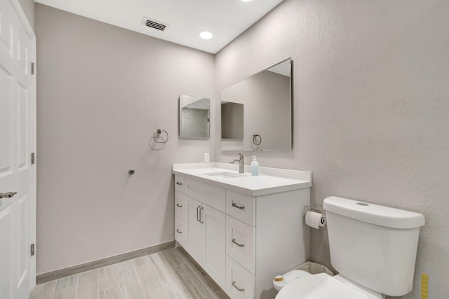 bathroom featuring vanity, baseboards, visible vents, wood finish floors, and toilet