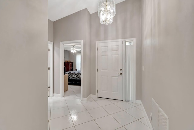 foyer entrance featuring visible vents, ceiling fan with notable chandelier, light tile patterned floors, baseboards, and a towering ceiling