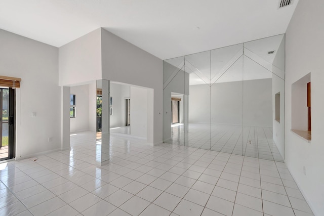 empty room featuring a high ceiling, light tile patterned flooring, and visible vents