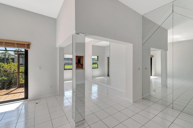 unfurnished room featuring light tile patterned flooring, baseboards, plenty of natural light, and a towering ceiling