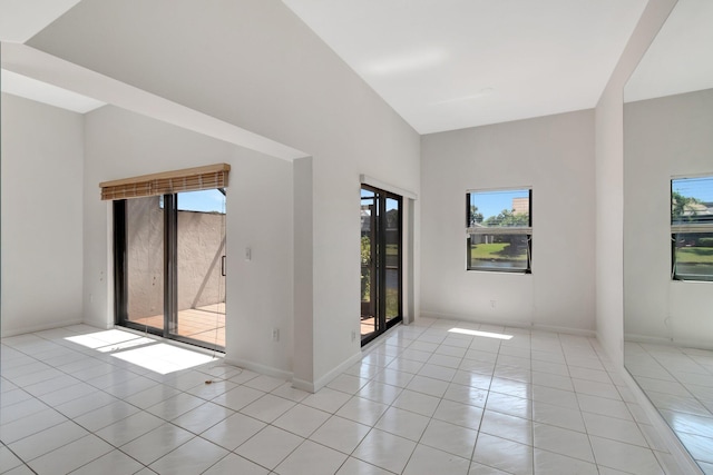 empty room featuring a high ceiling, light tile patterned flooring, and baseboards