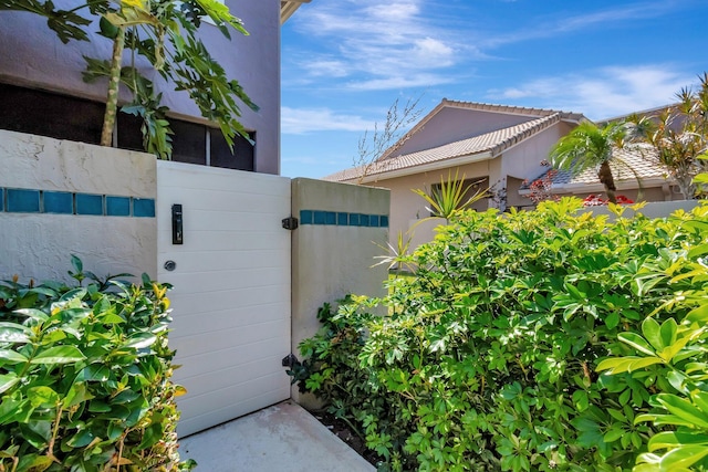 exterior space featuring stucco siding, a tiled roof, fence, and a gate