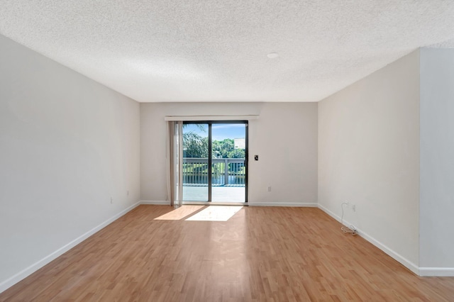 spare room with light wood-style floors, baseboards, and a textured ceiling