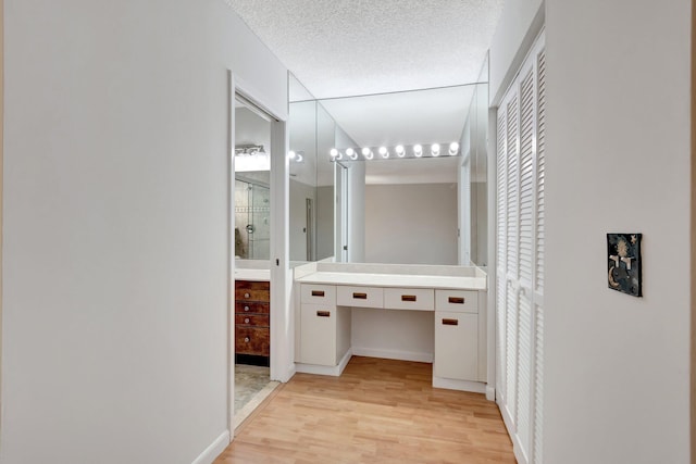 bathroom featuring baseboards, walk in shower, vanity, wood finished floors, and a textured ceiling