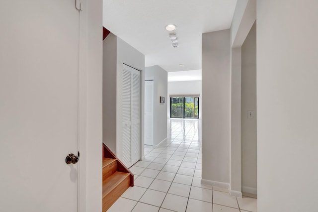 corridor featuring stairway, light tile patterned floors, and baseboards