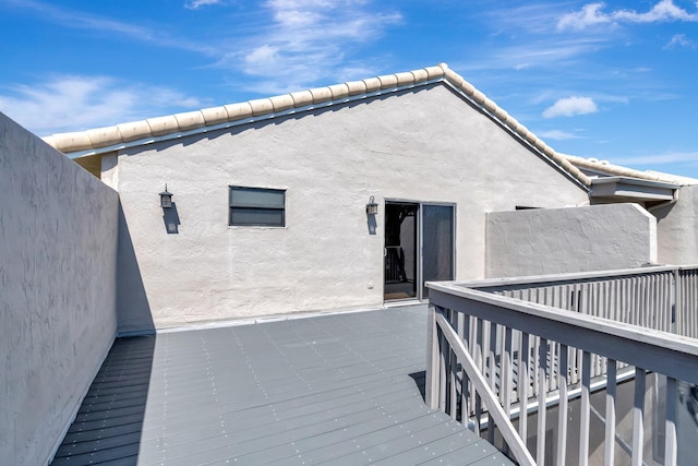 rear view of property with stucco siding, a tile roof, and a deck