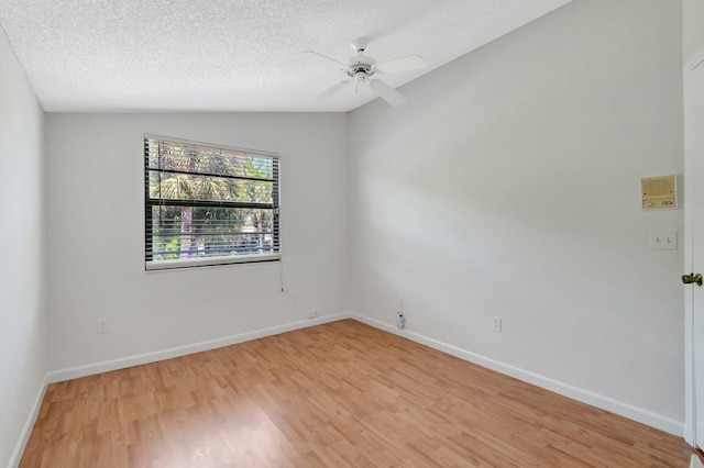 empty room with a textured ceiling, light wood-style floors, baseboards, ceiling fan, and vaulted ceiling