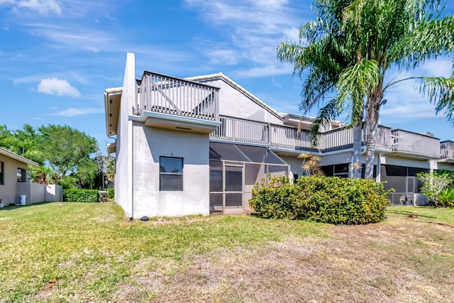 rear view of house featuring a lanai, a lawn, and stucco siding