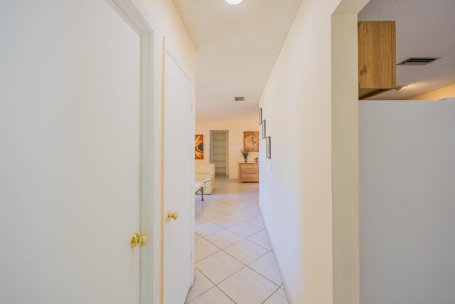 hall with light tile patterned flooring, visible vents, and a textured ceiling