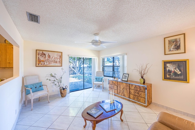 living area featuring light tile patterned floors, a ceiling fan, visible vents, and a textured ceiling