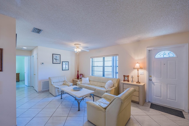 living area featuring light tile patterned floors, visible vents, a textured ceiling, and ceiling fan