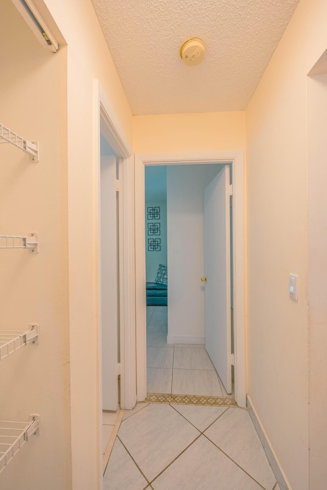 corridor with tile patterned flooring, baseboards, and a textured ceiling