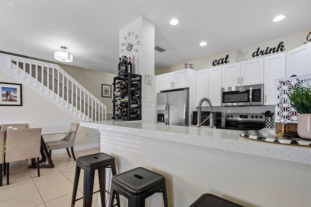 kitchen with light tile patterned floors, light stone countertops, stainless steel appliances, and a peninsula