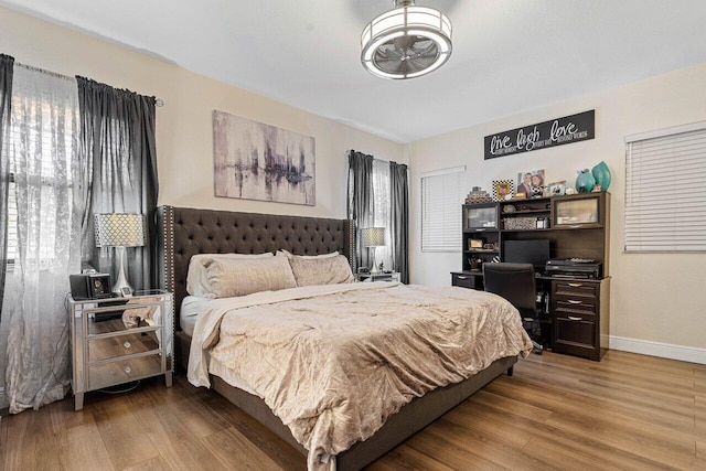 bedroom with multiple windows, wood finished floors, and baseboards