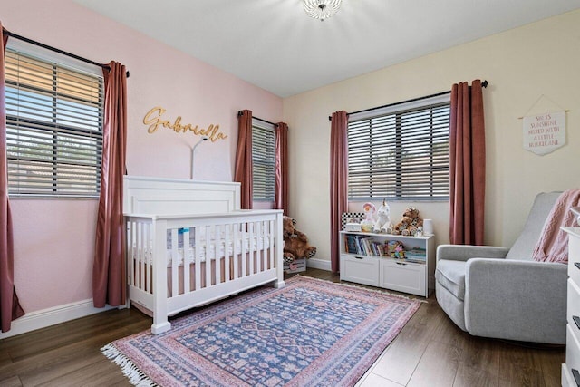 bedroom featuring baseboards, wood finished floors, and a nursery area