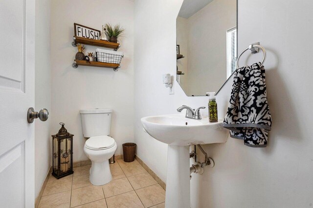 half bathroom with baseboards, toilet, and tile patterned flooring