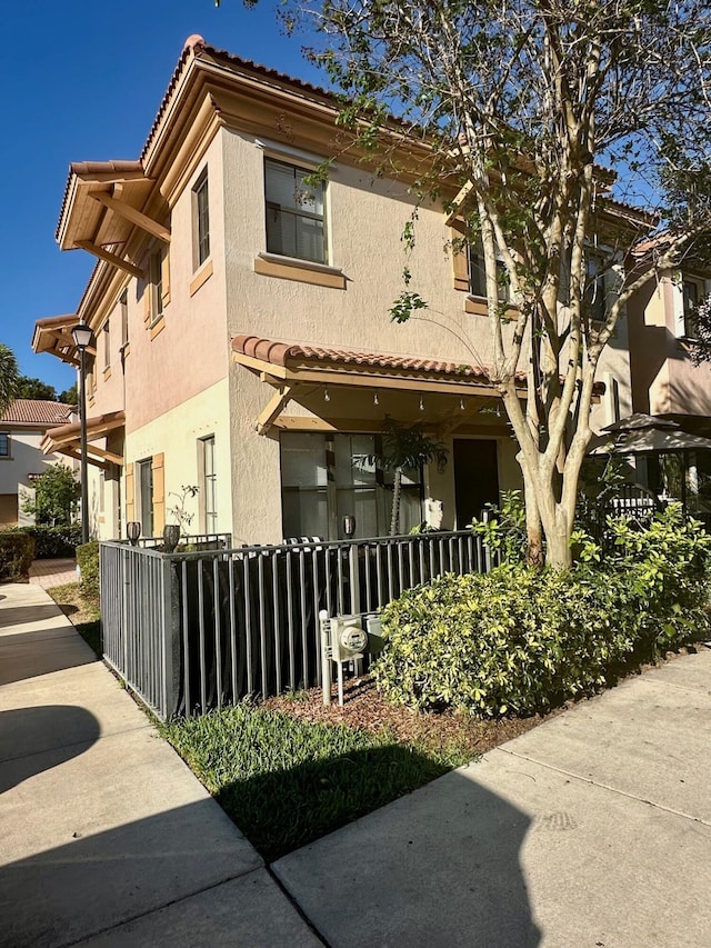 view of front facade featuring covered porch, stucco siding, a tiled roof, and fence