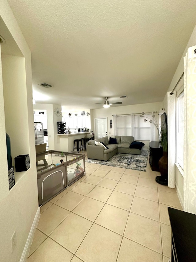 living room featuring light tile patterned flooring, a ceiling fan, visible vents, and a textured ceiling