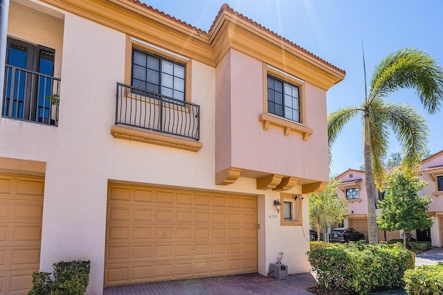 view of front of house featuring a balcony, a tiled roof, stucco siding, and an attached garage