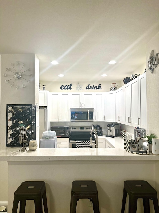 kitchen featuring stainless steel appliances, backsplash, a peninsula, and white cabinets