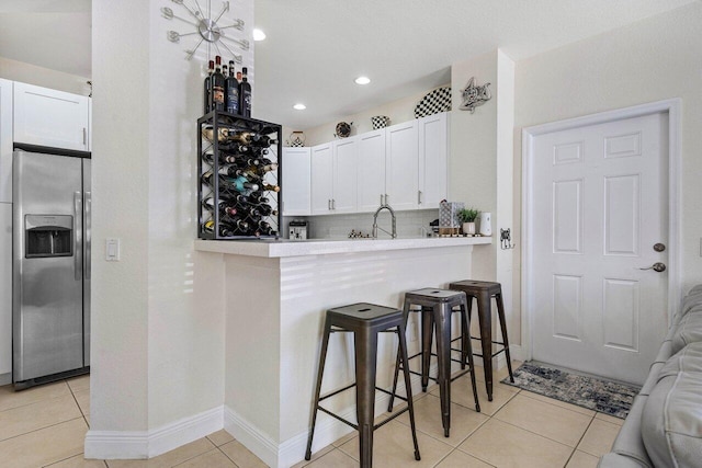 kitchen with stainless steel fridge with ice dispenser, white cabinets, a kitchen bar, and light tile patterned floors