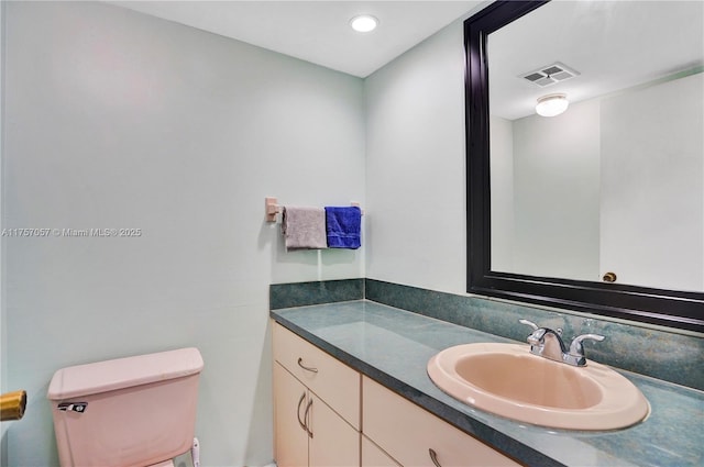 half bath featuring vanity, toilet, and visible vents